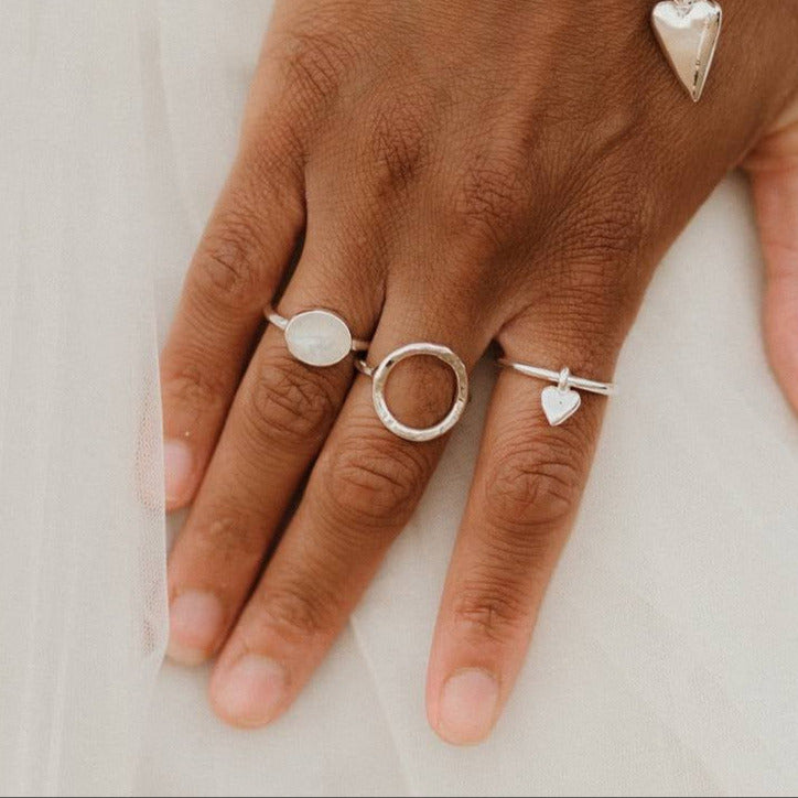 A person's hand wearing a silver hammered ring along with other silver rings and bracelets.