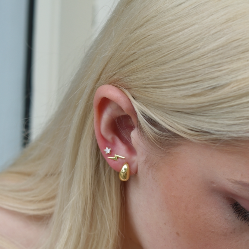 Close-up of a person wearing gold earrings with a neutral background