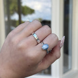 Hand wearing two rings with a blue gemstone in front of a glass door.