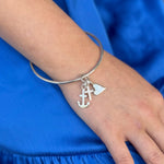 Silver bracelet with anchor charm on a wrist against a blue background