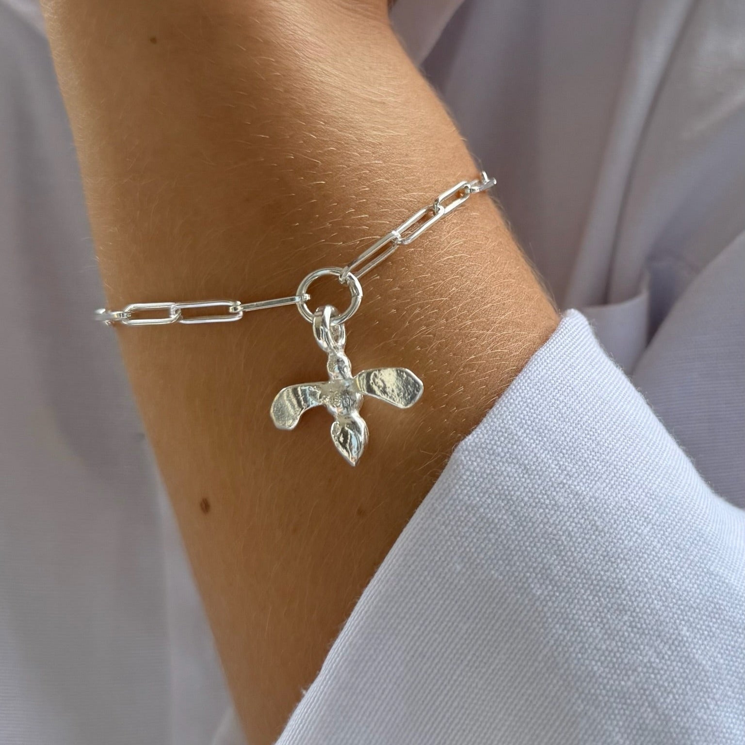 Silver bracelet with a cross charm on a wrist against a white background