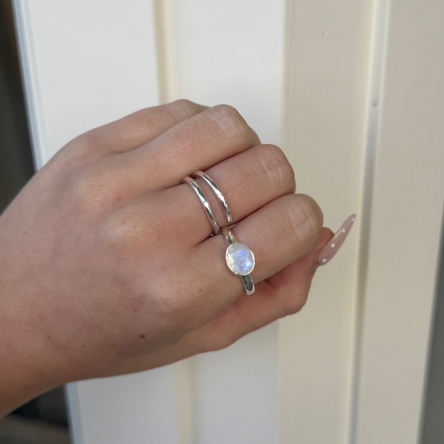 Hand wearing a silver ring with a moonstone on a neutral background