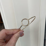 Hand holding a small metallic clip against a white curtain background
