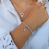 Silver heart-shaped bracelet on a wrist with a blurred white background